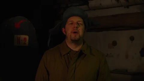 Russian man in a hat with earflaps, talking on the phone in a dark basement and Video stock 107324278