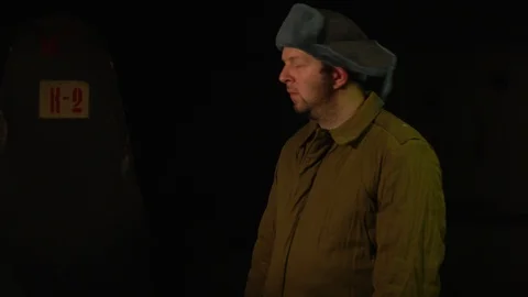 Russian man in a hat with earflaps, talking on the phone in a dark basement and Video stock 107324933