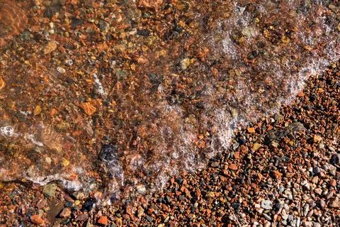 Rust-colored pebbles with foamy water edge Stock Photos