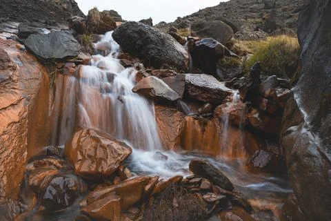Rust-colored waterfall flows through volcanic rocks in Iceland wild highlands Foto stock