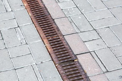 A rust lattice of a drainage paving system on walkway made of square stone. Stock Photos