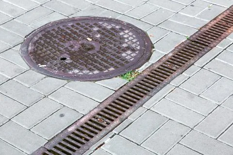 A rust lattice of a drainage paving system and round sewer manhole. Stock Photos