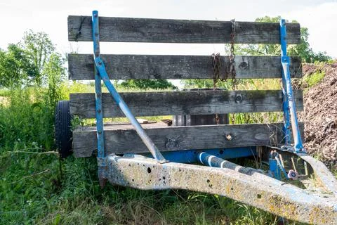 Rusted and worn down flat bed trailer with weeds overgrowing. Stock Photos