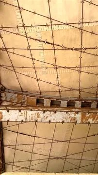 Rusted beams intersect across geometric ceiling in abandoned desert structure Stock Photos