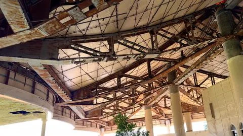 Rusted beams support geometric ceiling over worn outdoor walkway in abandoned Stock Photos