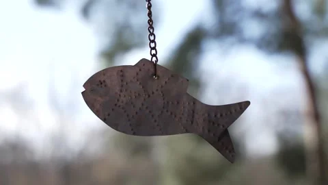 Rusted fish hangs from a chain against a blurred forest backdrop Stock Footage 331701991
