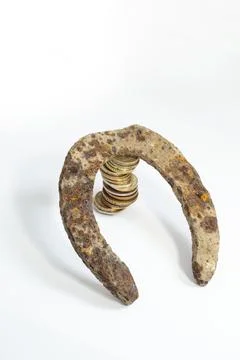Rusted horse shoe leaning on a stack of golden coins Stock-Fotos