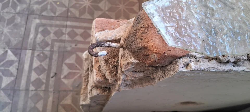 Rusted metal hook embedded in a weathered red brick wall structure Stock Photos