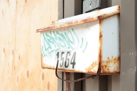 Rusted old beat up rusty worn dented bent white mailbox with green graffiti Stock Photos