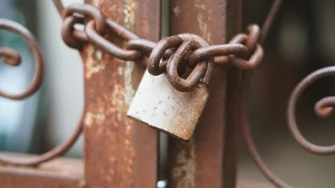 A rusted padlock securing an aged metal gate with ornate scrollwork Stock Photos