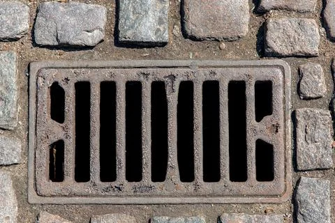Rusted rectangular grating manhole drainage system on the pavement road. Stock Photos