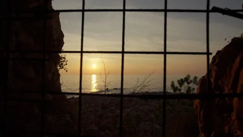 A rusted square grate frames a golden sunset on the Adriatic in Montenegro, with Stock Footage 329411964