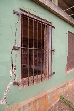 Rusted steel gate blocking window in dilapidated building with concrete falling Stock Photos