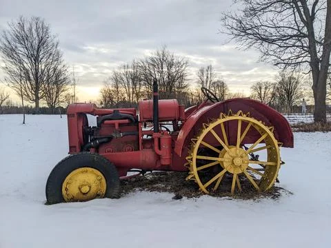 Rustic antique red tractor parked in a snow-covered meadow Foto stock