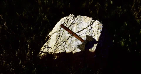 Rustic axe resting on a weathered stone in a grassy setting at dusk Stock Footage 313655529