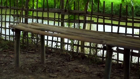 Rustic bamboo bench beside a peaceful pond in a rural countryside setting Видео 339759452