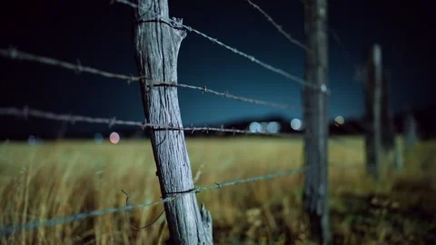 Rustic Barbed Wire Fence Post in Rural Field at Night with Bokeh Lights. Stock Footage 337908659