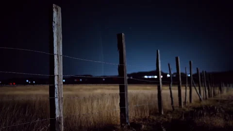 Rustic Barbed Wire Fence in Rural Field at Night with Distant City Lights. Stock Footage 337914416