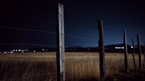 Rustic Barbed Wire Fence on Rural Prairie Field at Night with Distant City. Stock Footage 337916098