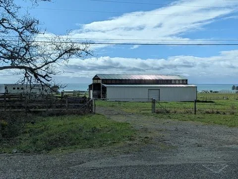 Rustic barn behind a gate with ocean visible in the distance Stock Photos