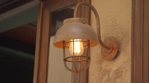 Rustic barn light fixture glows warmly on textured wall with wood trim. Video stock 332474812