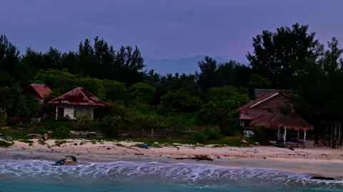 Rustic beach bungalows at dusk on tropical islands shore with mountain Видео 334267222