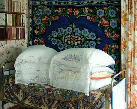 Rustic bed with pillows on the background of the carpet and bookshelves Stock Photos