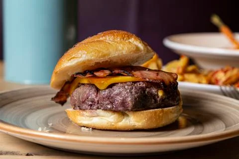 Rustic beef burger with cheese and bacon served on a plate. Stock Photos