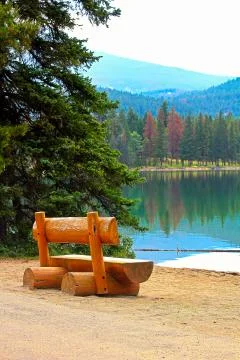 A rustic bench sits on a calm lake shore in the mountains Stock Photos
