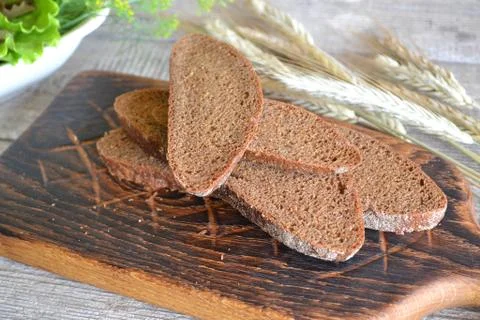 Rustic black bread and wheat on an old vintage planked wooden table. Stock Photos