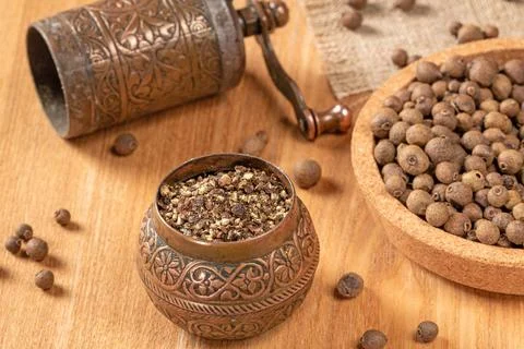 Rustic black pepper mill and whole peppercorns on wooden background Stock Photos