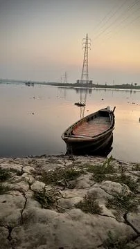 Rustic Boat on a Calm River at Dusk with Power Lines. boats at sunset. Stock Photos