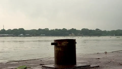 Rustic bollard by a tranquil riverbank under a cloudy sky with distant greene Vídeos de archivo 340221605