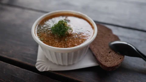 Rustic bowl of hot soup with fresh dill, bread slice, and spoon on dark wooden Stock Footage 344772500