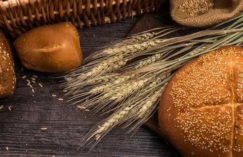 Rustic bread and wheat stalks on a dark wooden surface Stock Photos