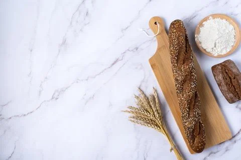 Rustic bread roll or french baguette, wheat and flour on a light background. Stock Photos