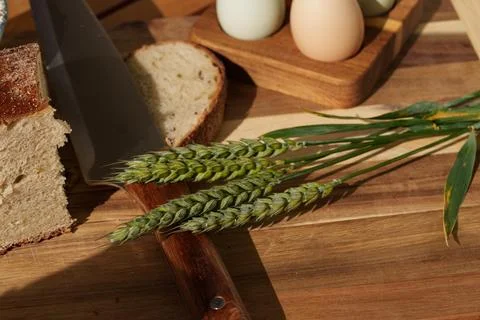 Rustic bread slicing scene with wheat stalks, eggs on wooden tray, and knife on Stock Photos