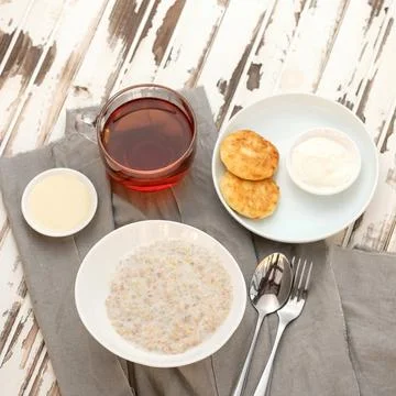 Rustic breakfast. Oatmeal, tea and cheesecakes with sour cream on wooden table Stock Photos