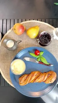 Rustic breakfast setup featuring blue plate with flaky pastry, fresh basil Stock Photos