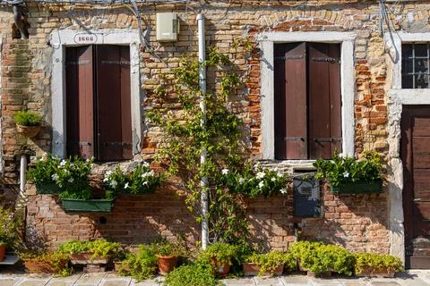Rustic brick facade with flower boxes and shuttered windows in Venice. A Stock Photos