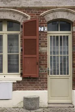 A rustic brick wall presents a beautifully shuttered window, paired with a ch Stock Photos