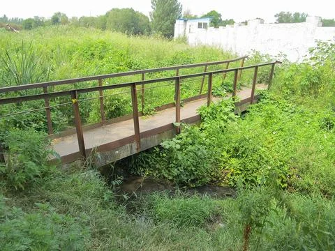A rustic bridge crosses over a stream or river surrounded by lush, overgrow.. Stock Photos