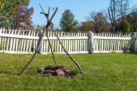 Rustic campfire with colonial cooking cauldron tripod in green grass Stock Photos