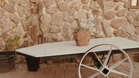Rustic Cart Table with Flower Basket Against a Stone Wall on a Patio Stock Footage 344013387