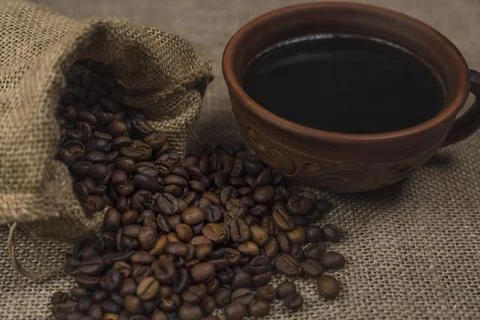 Rustic ceramic cup of black coffee with burlap sack spilling coffee beans Stock Photos