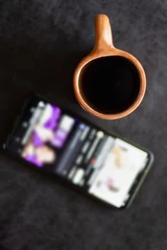 A rustic clay cup filled with hot coffee next to a cell phone Stock Photos