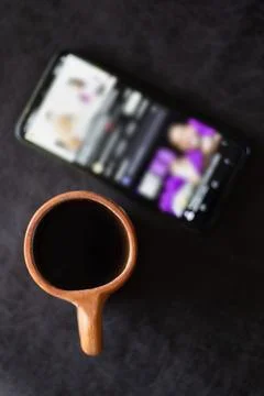 A rustic clay cup filled with hot coffee next to a cell phone Stock Photos