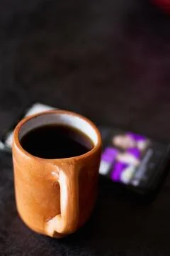 A rustic clay cup filled with hot coffee next to a cell phone Stock Photos