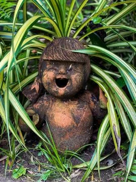 Rustic Clay Doll Statue Amidst Green Foliage in a Garden Stock Photos