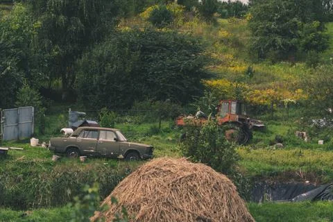 A rustic courtyard. A haystack. In the background is an old car and a tractor Stock Photos